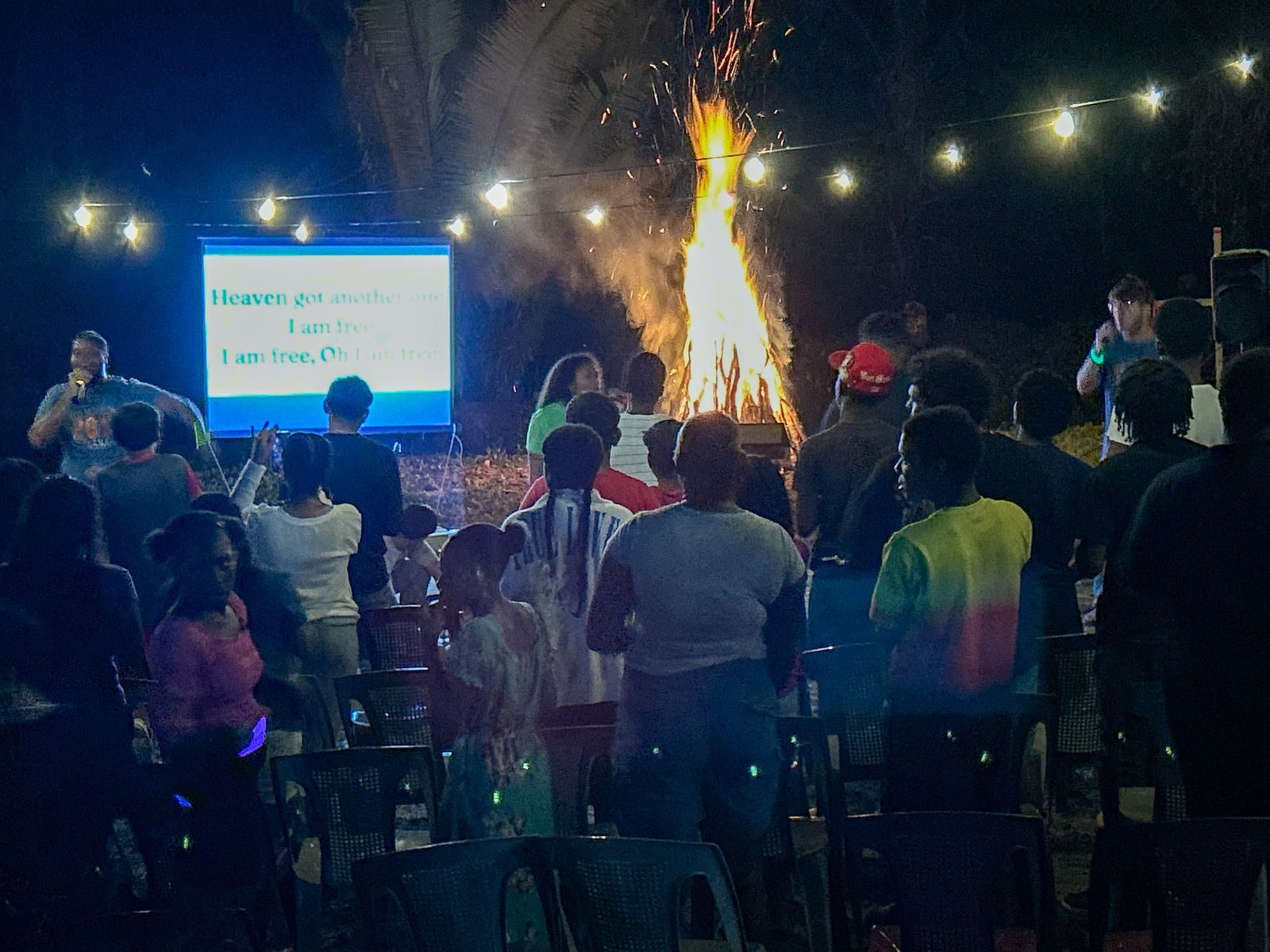 Group gathered around a bonfire and screen at night