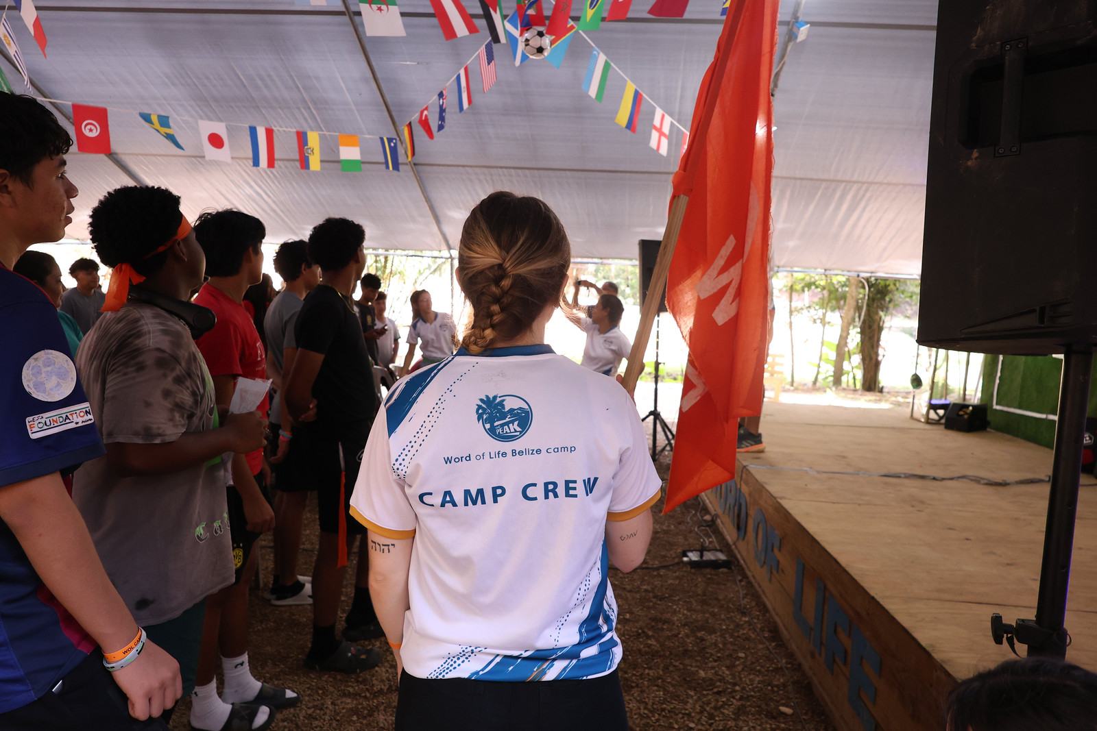 Camp Crew member in a Camp Crew shirt standing with campers by a team flag in the meeting tent