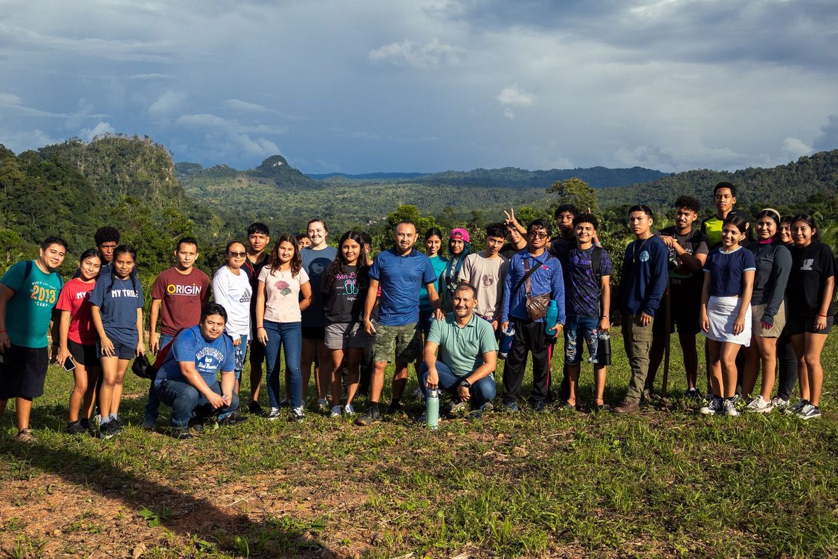 A group standing on a hilltop with green hills and mountains behind them